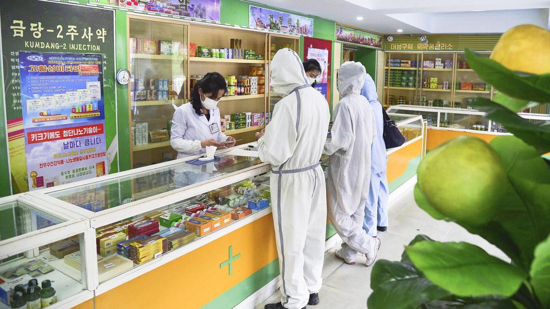 Фармацевт в маске и люди в защитных костюмах стоят в аптеке