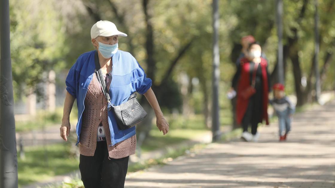 Женщина в маске и кепке идет по улице