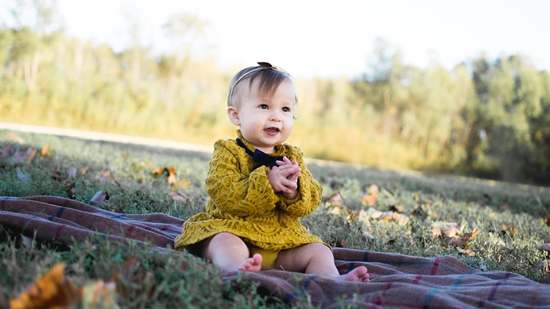 Маленькая девочка сидит на покрывале на поляне