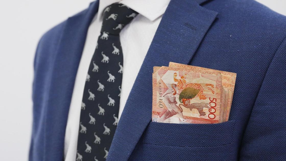 Пачка денег лежит у мужчины в переднем кармане делового костюма