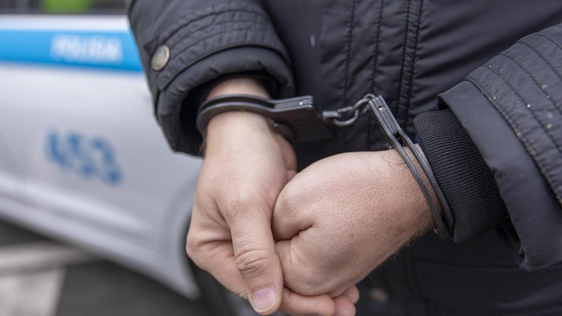 Задержанный в наручниках стоит у полицейского авто