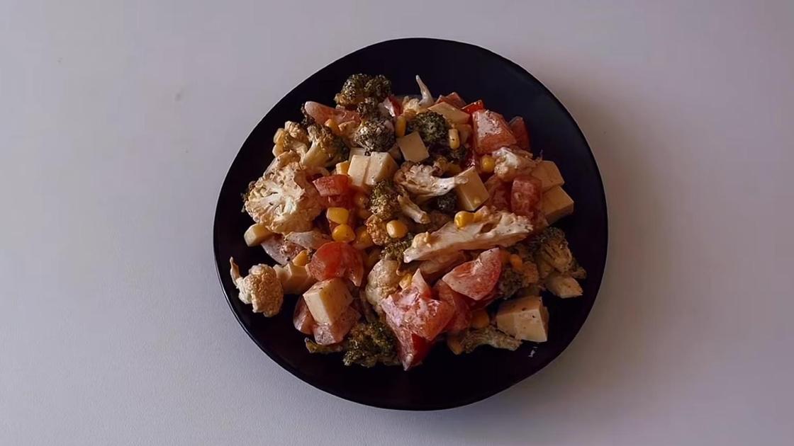 На сервировочной тарелке салат с капустой, помидорами и кукурузой