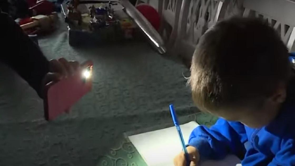 Ребенок делает уроки под свет фонарика на смартфоне