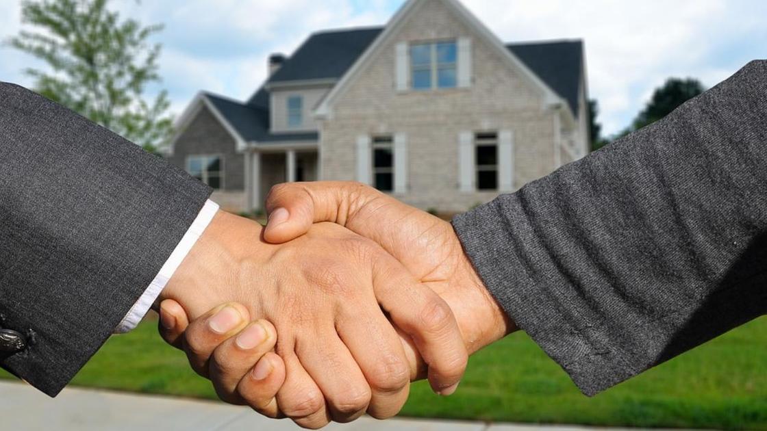 мужчины пожимают друг другу руки на фоне дома