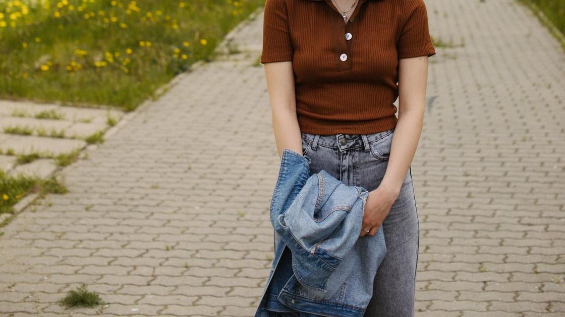 Девушка стоит на улице и держит в руках джинсовую куртку
