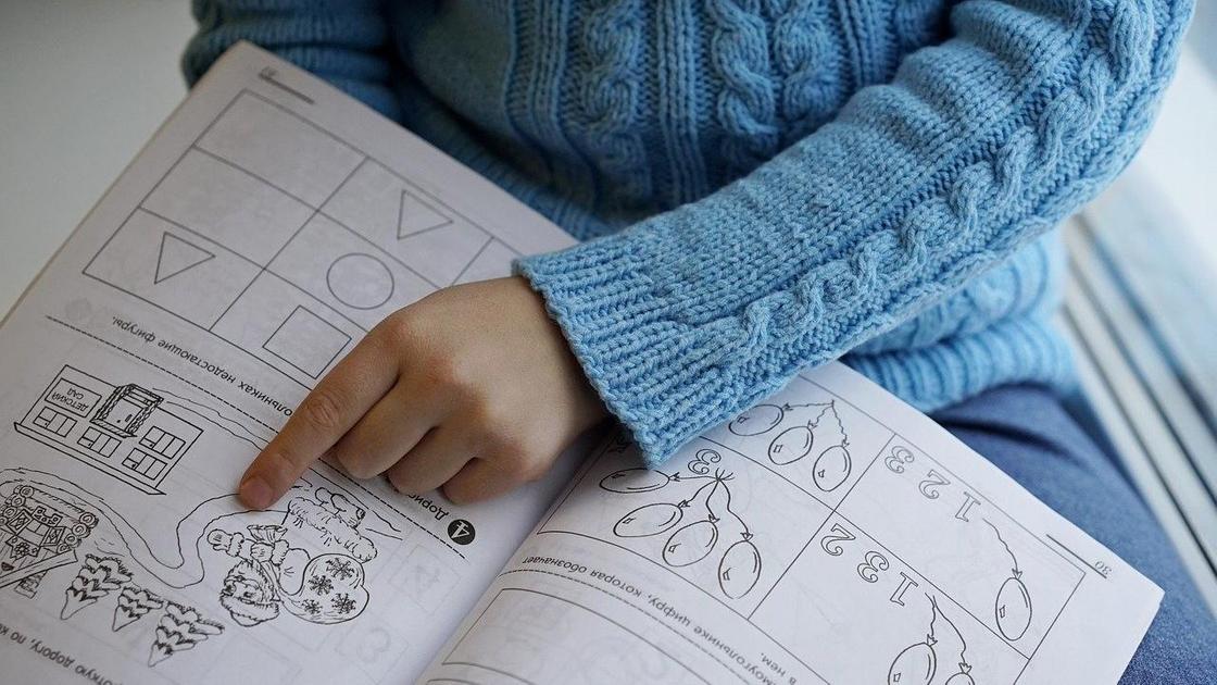 Ребенок показывает пальцем на задание в рабочей тетради