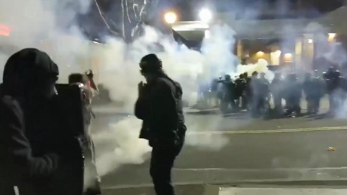 Две группы людей стоят друг напротив друга в дыму на улице