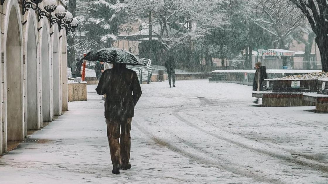 Мужчина идет с зонтом в снегопад