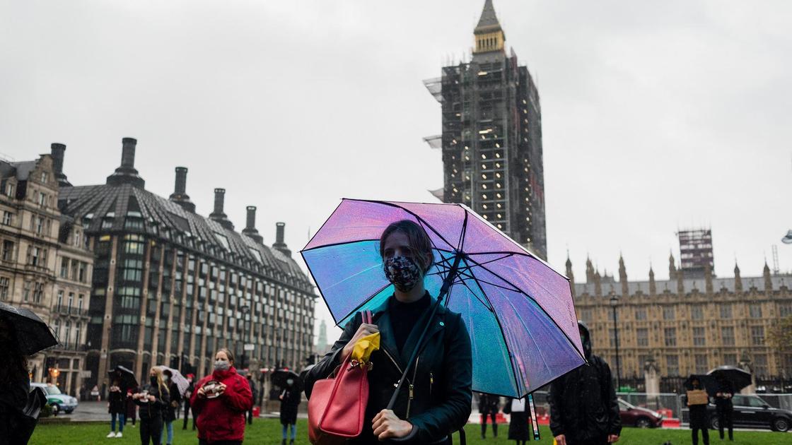 Девушка с зонтиком и в маске позирует на площади парламента в Лондоне