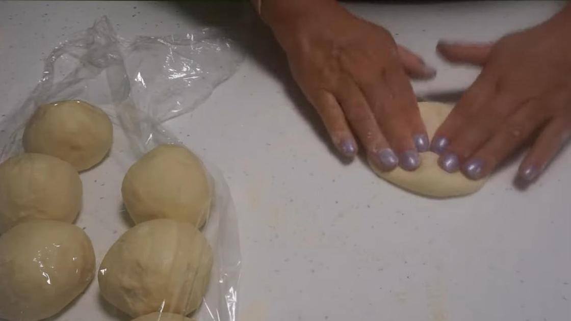 Заготовки на пирожки в виде шариков теста под пищевой пленкой на столе