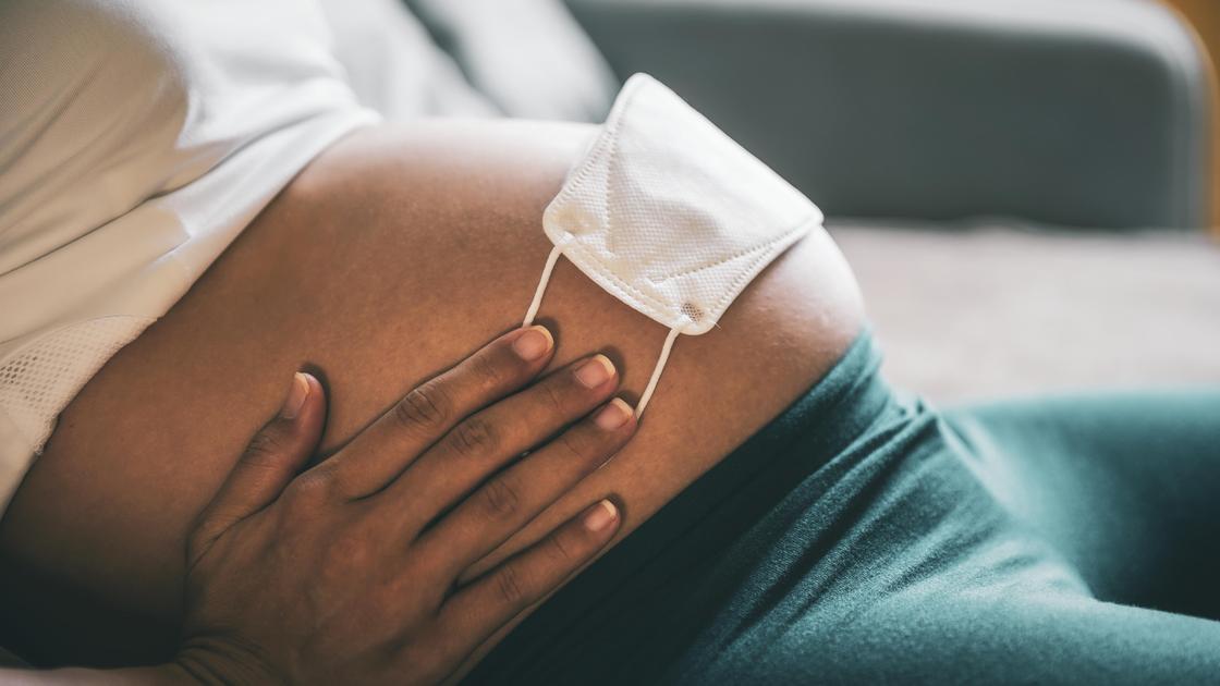 Беременная женщина держит руками медмаску на животе
