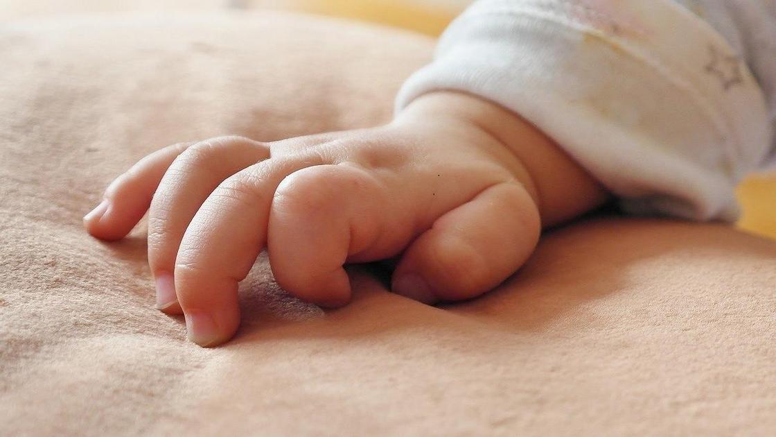 Младенец положил руку на одеяло