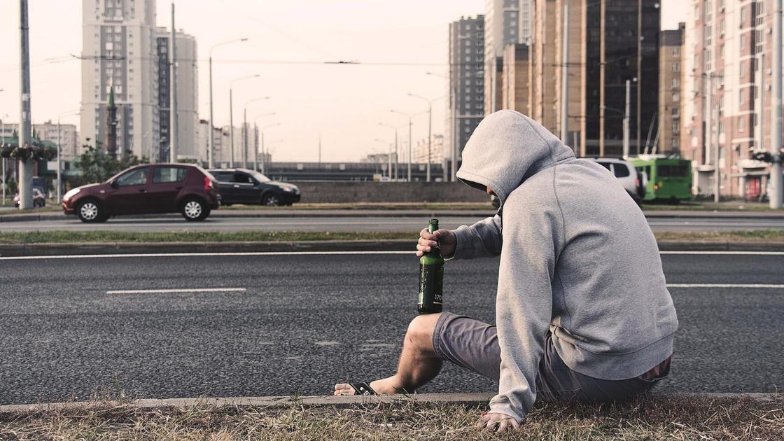 Мужчина сидит на дороге с алкоголем