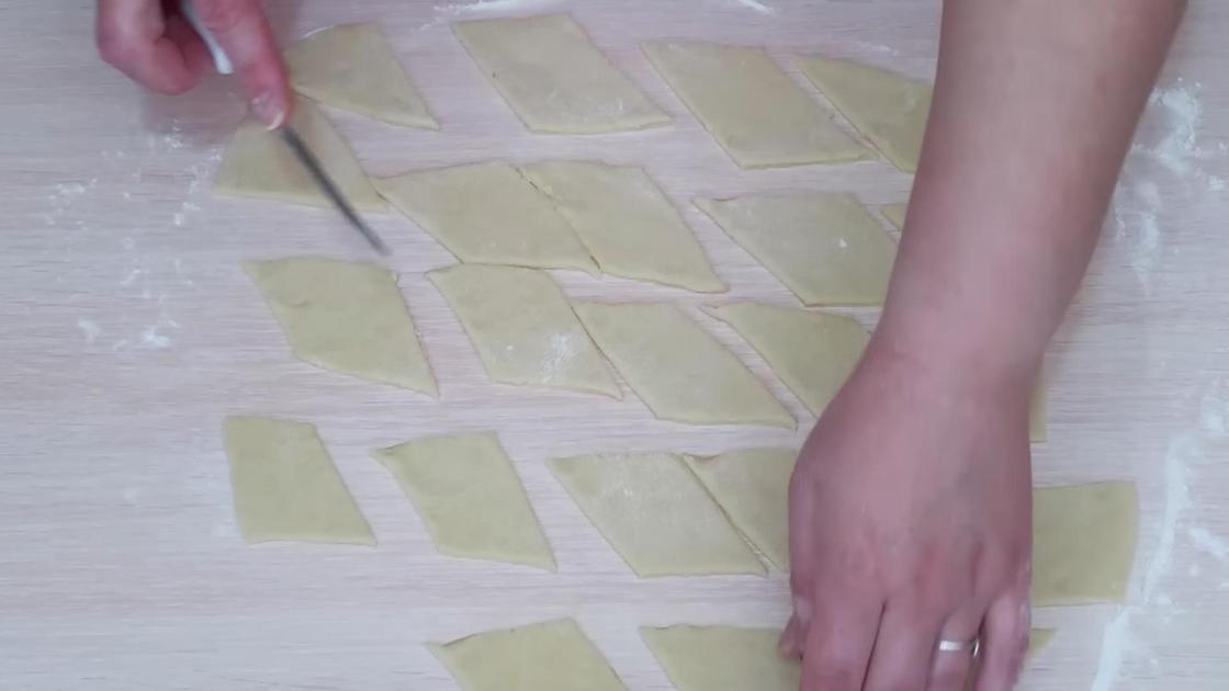 Женские руки нарезают тесто на заготовки для хвороста ромбиками