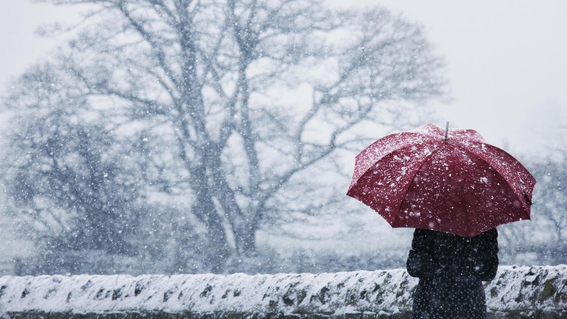 Человек стоит с зонтом под снегом