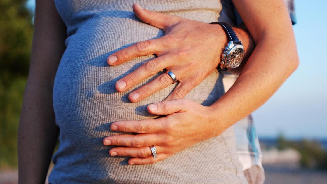 Беременная женщина держит руками живот