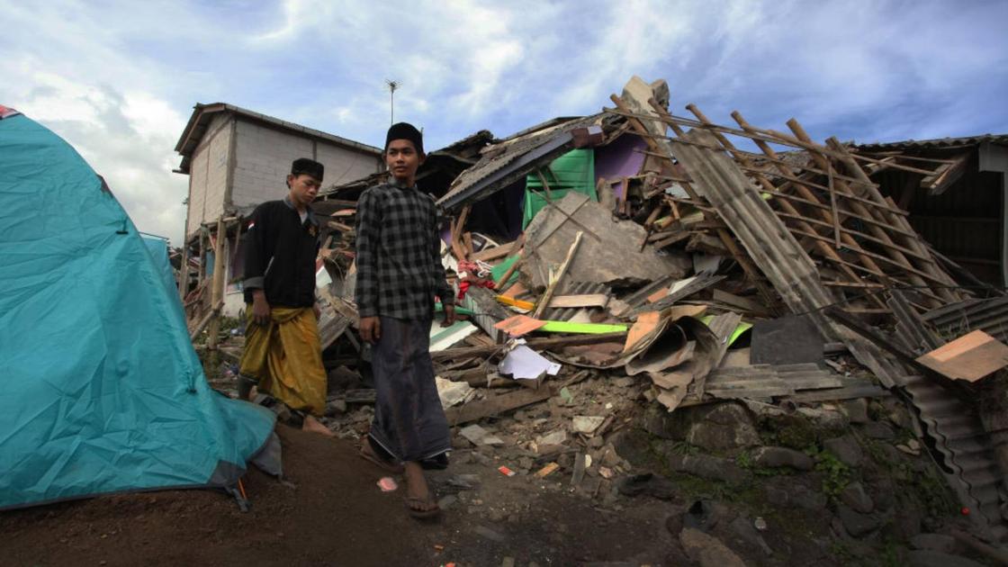 Люди рядом с разрушенным после землетрясения домом в Индонезии