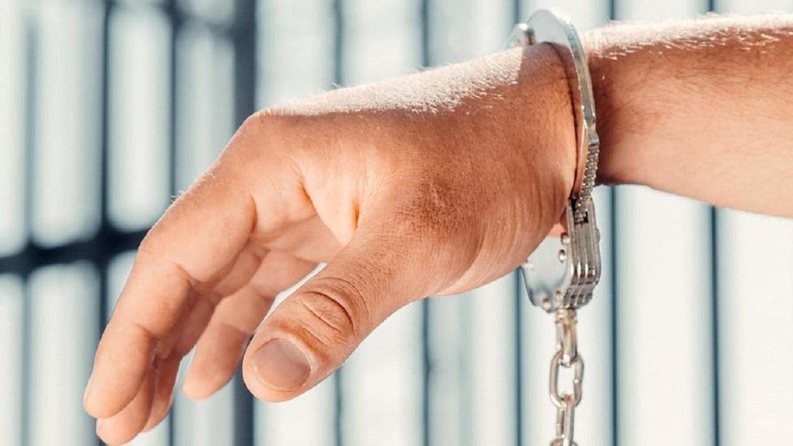 Рука в наручниках на фоне решетки
