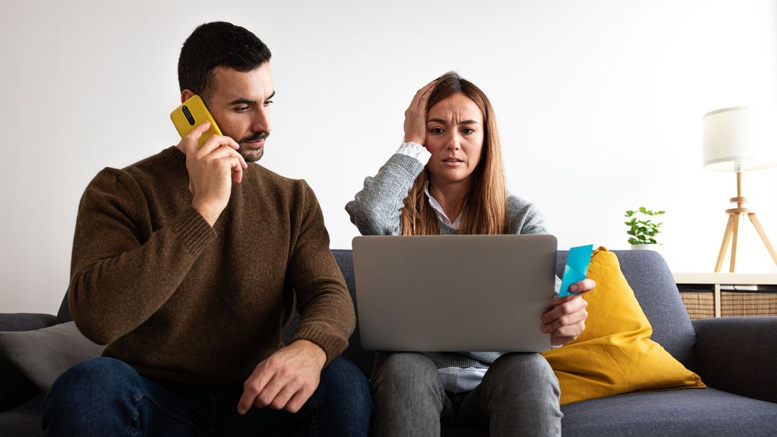 Молодая пара. Мужчина звонит по телефону, а женщина с ноутбуком сидит в растерянности