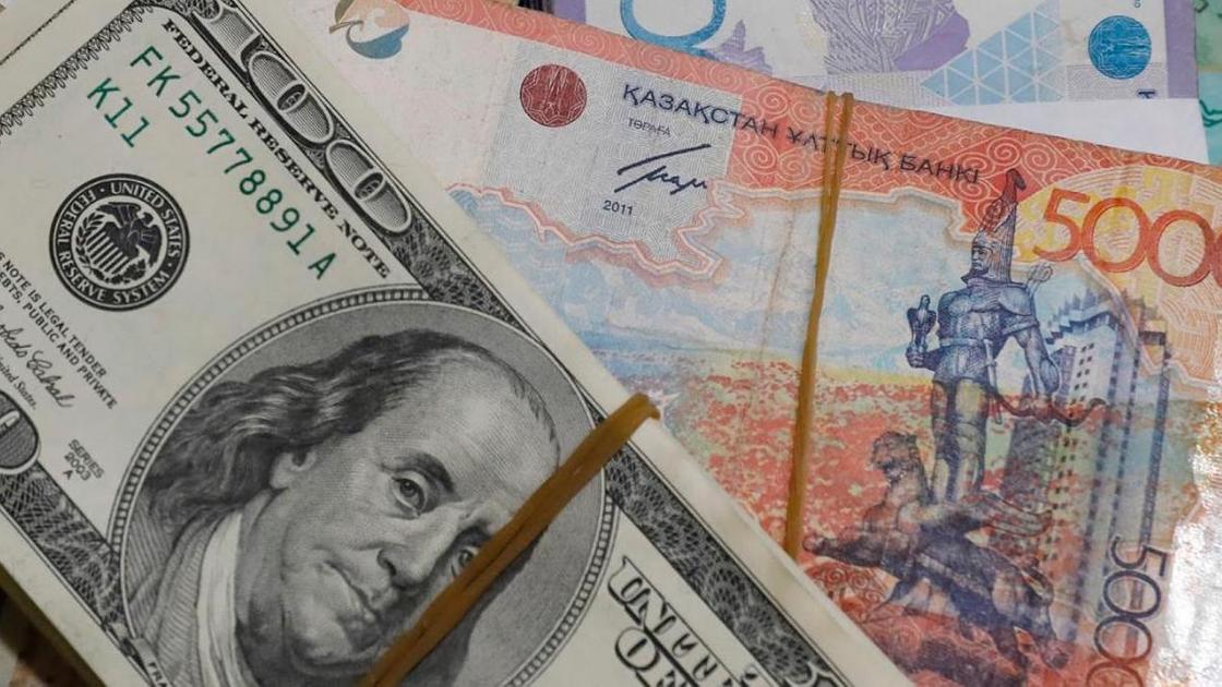 Пачка долларов лежит среди пачек тенге