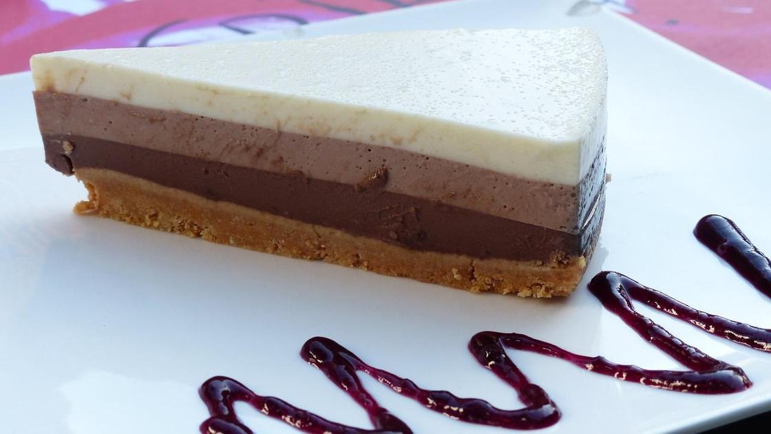 Кусочек торта «Три шоколада» на белой тарелке с украшением