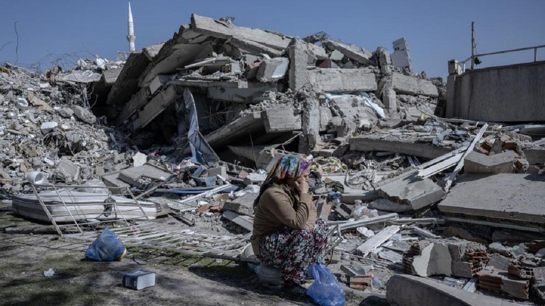 Женщина сидит на фоне разрушенного дома в Турции