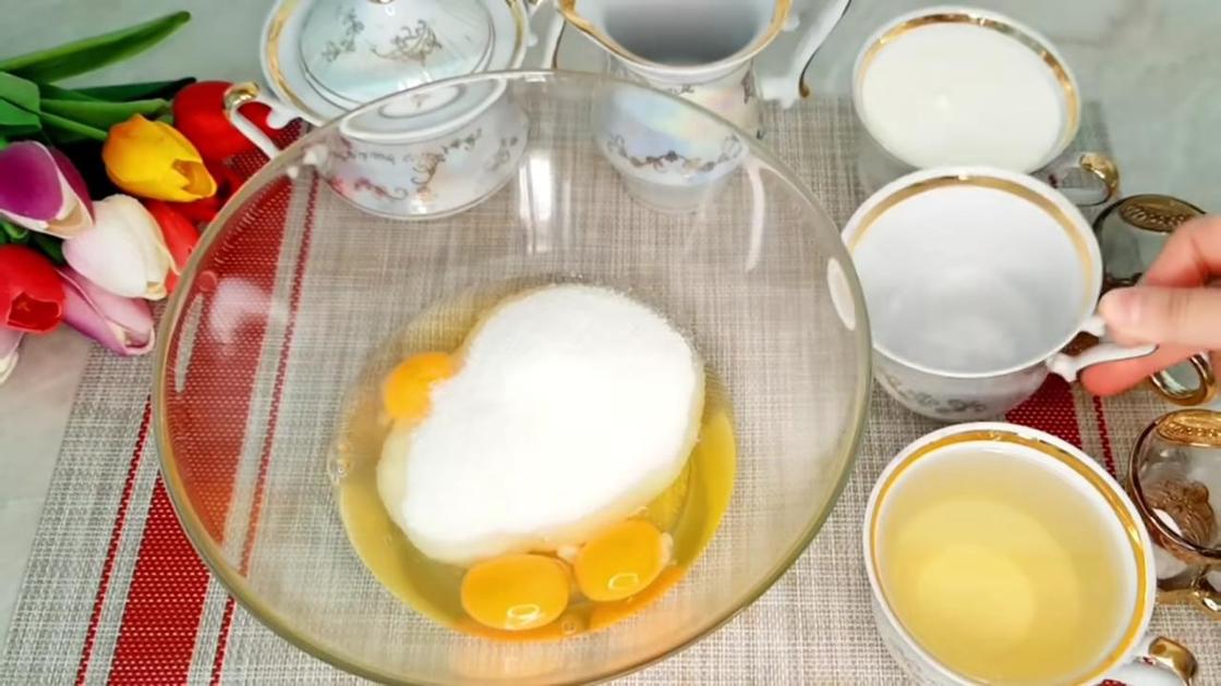 В стеклянной миске разбиты яйца и насыпан сахар