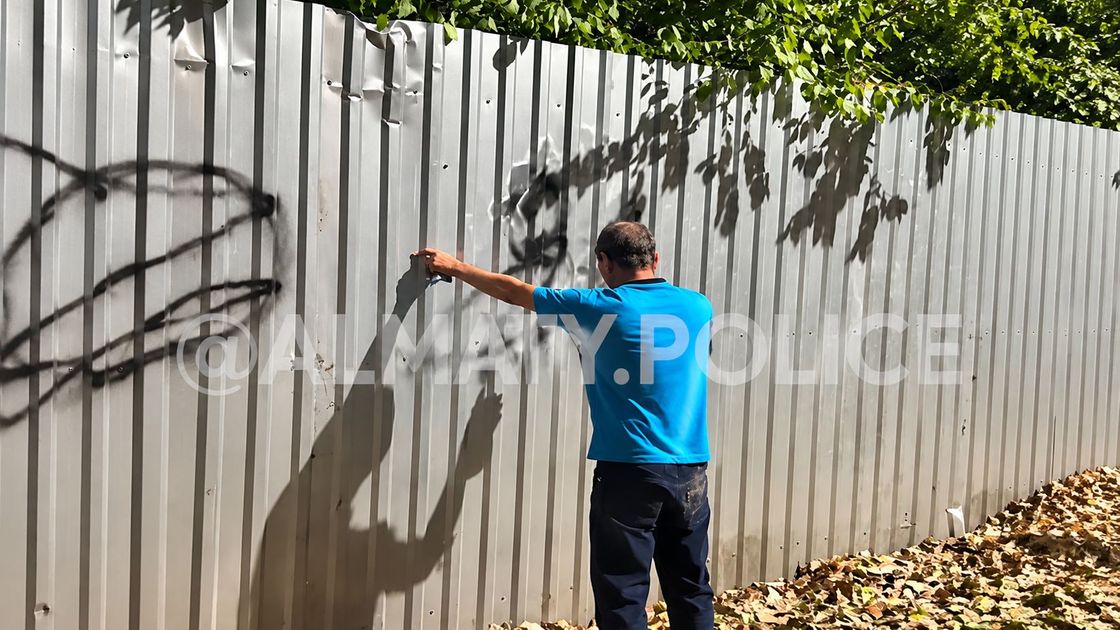 Мужчина наносит надпись на забор