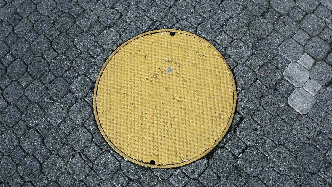 Желтый канализационный люк, расположенный посреди тротуара