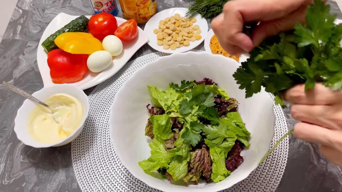 Салатница с листьями салата и петрушки. Рядом тарелка с майонезом и свежими овощами