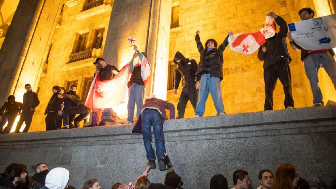 Молодые люди с флагами Грузии стоят на стене