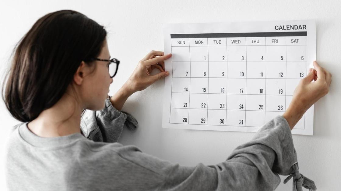 Девушка вешает на стену чистый лист календаря