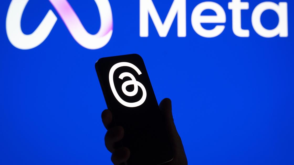 Человек держит смартфон с логотипом Threads на фоне логотипа Meta
