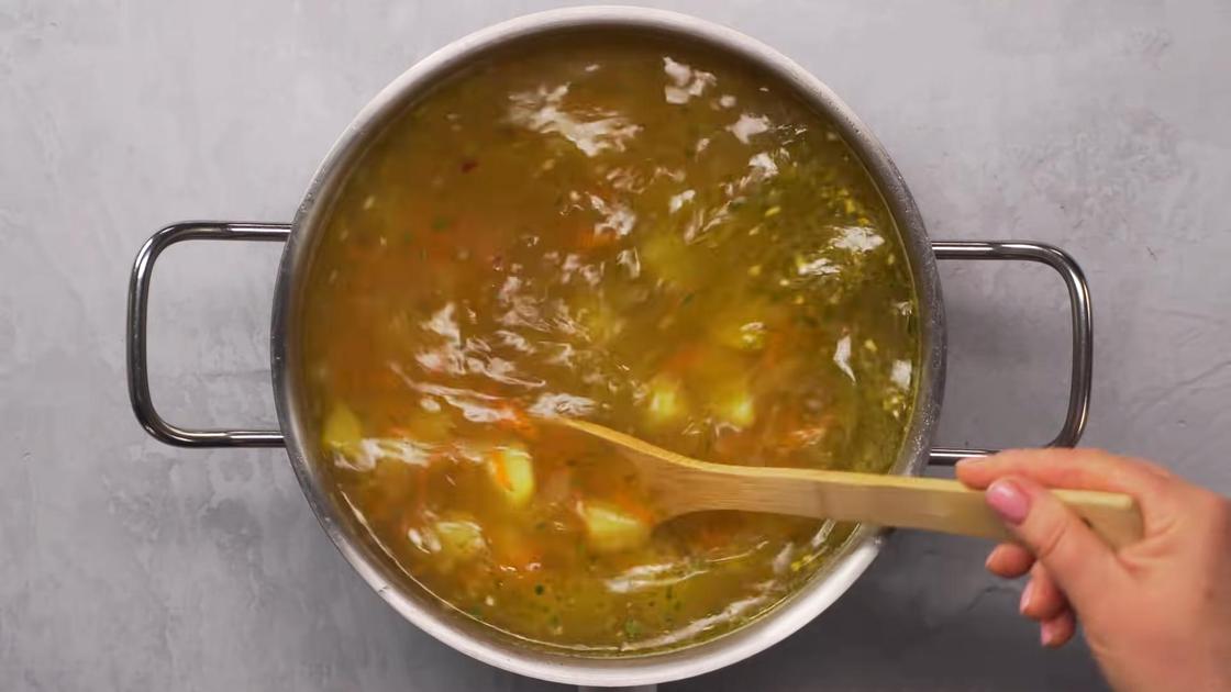 Ингредиенты супа перемешивают в кастрюле деревянной лопаткой