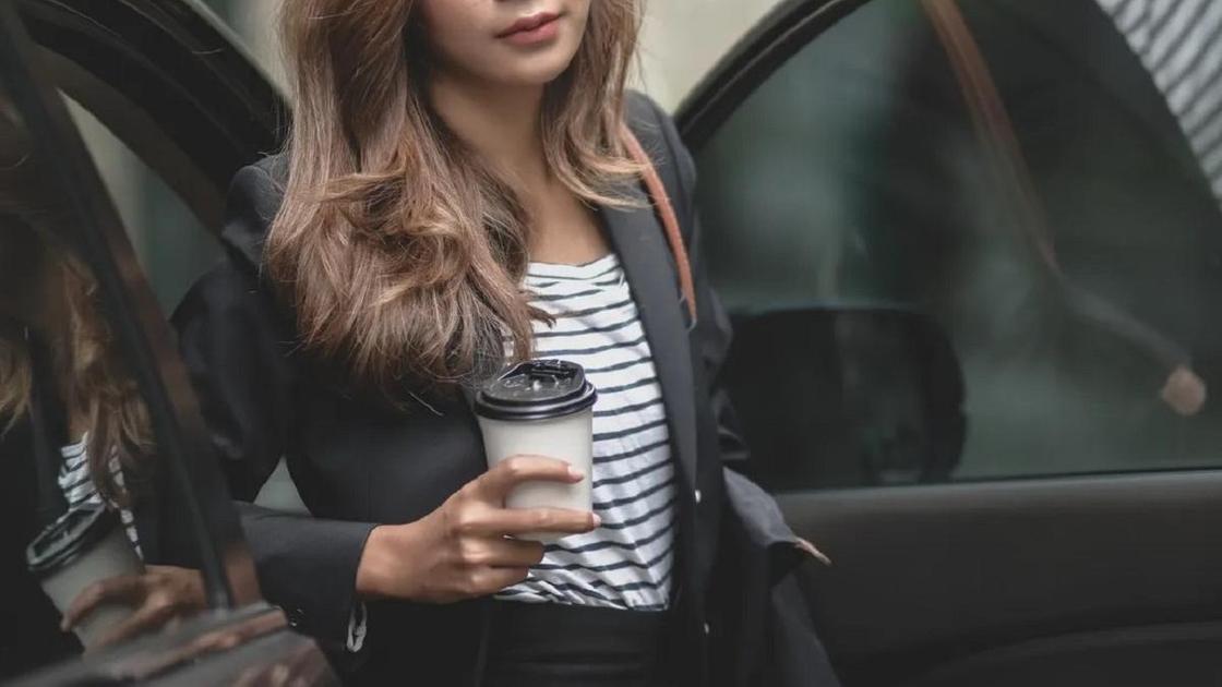 Девушка выходит из автомобиля с кофе в руке