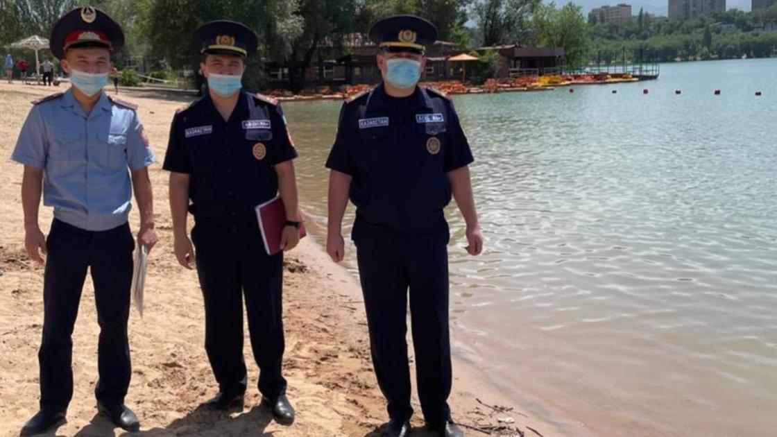 Полицейский и два сотрудника ДЧС стоят у озера Сайран