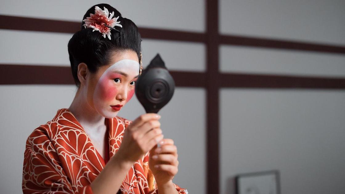 Девушка в костюме гейши смотрит в зеркальце