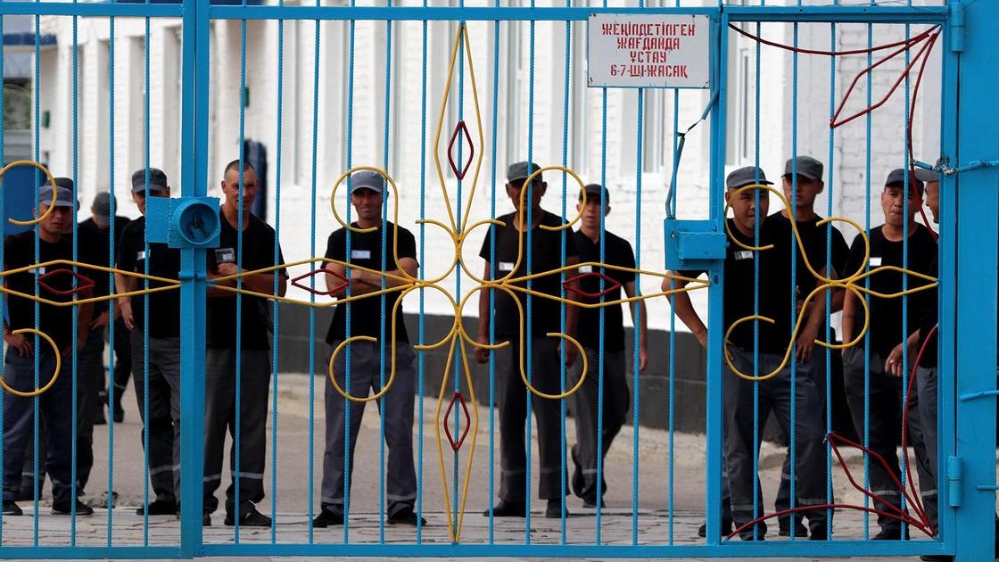Заключенные стоят за воротами колонии