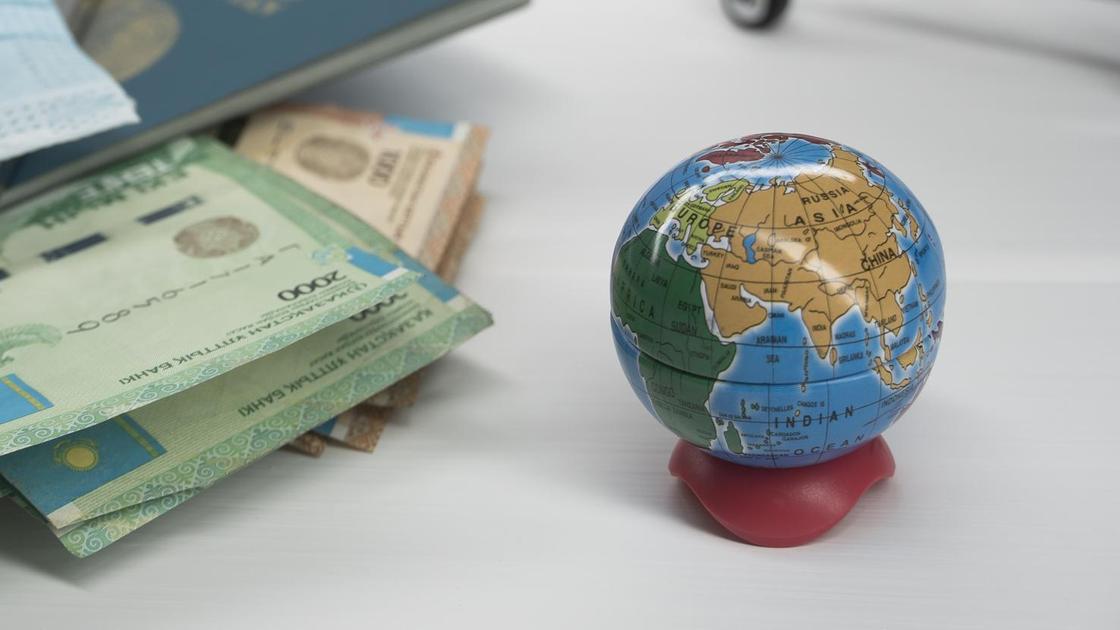 Меленькая модель земли стоит рядом с кошельком с тенге