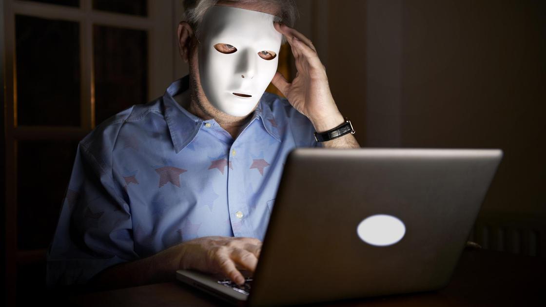 Человек в маске сидит за ноутбуком