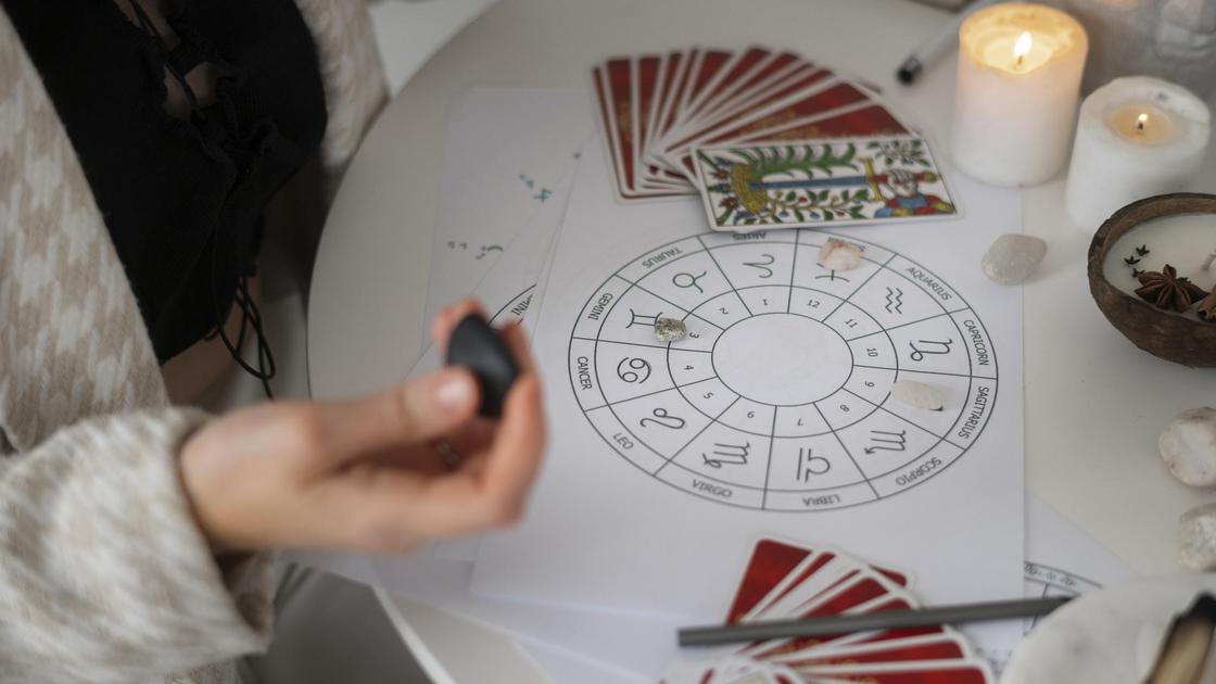 Таролог раскладывает карты и камни на изображении знаков зодиака