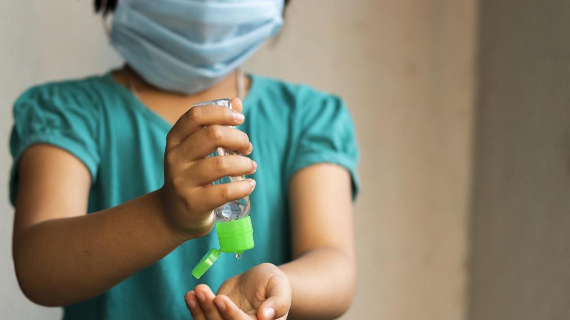 Ребенок в маске обрабатывает руки антисептиком