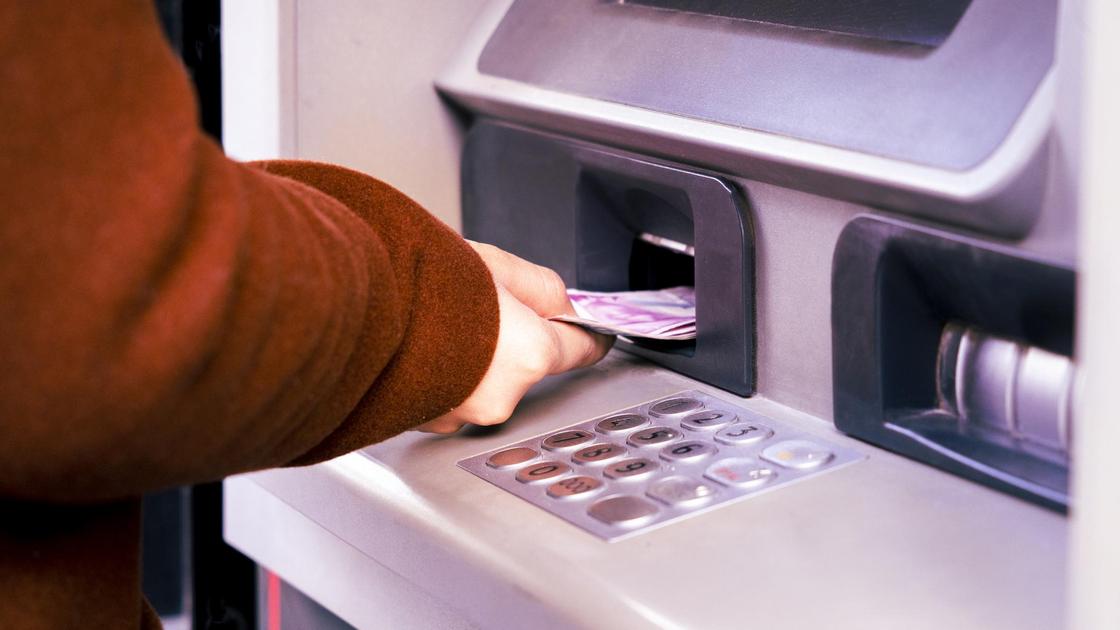 Женщина кладет деньги на счет через банкомат