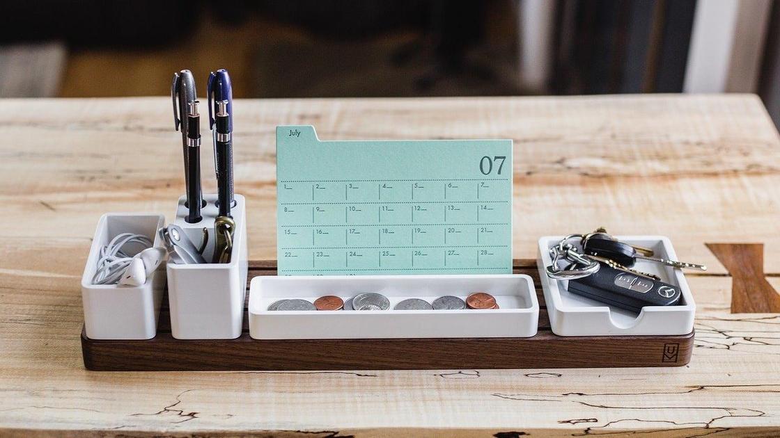На столе стоит календарь и органайзер с ручками