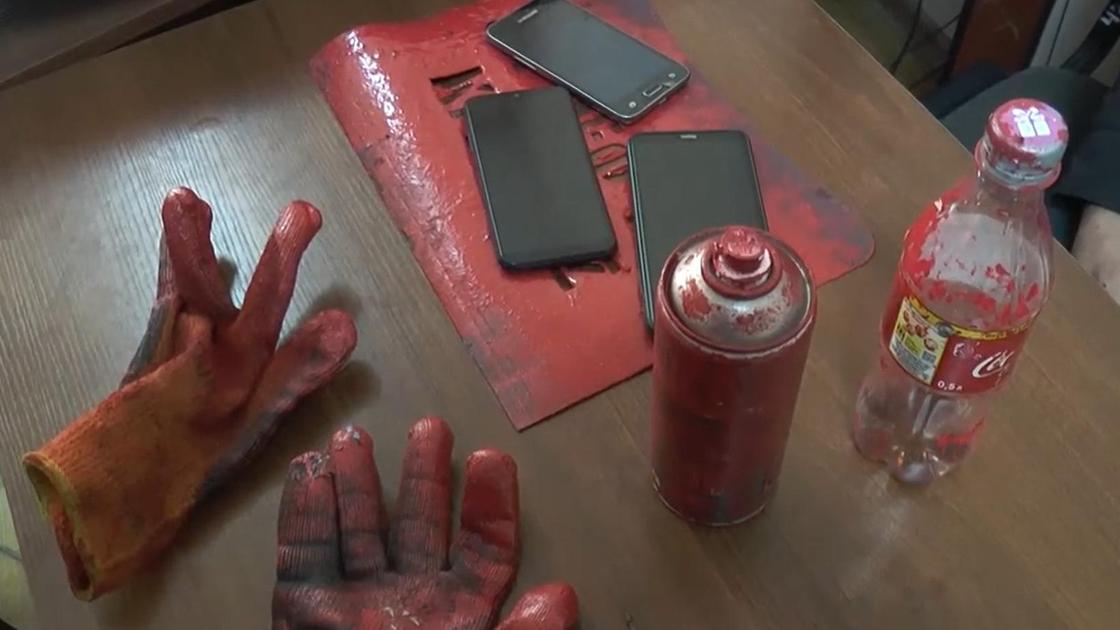 Перчатки, трафарет, два смартфона, баллончик с красной краской и пластиковая бутылка на деревянном столе