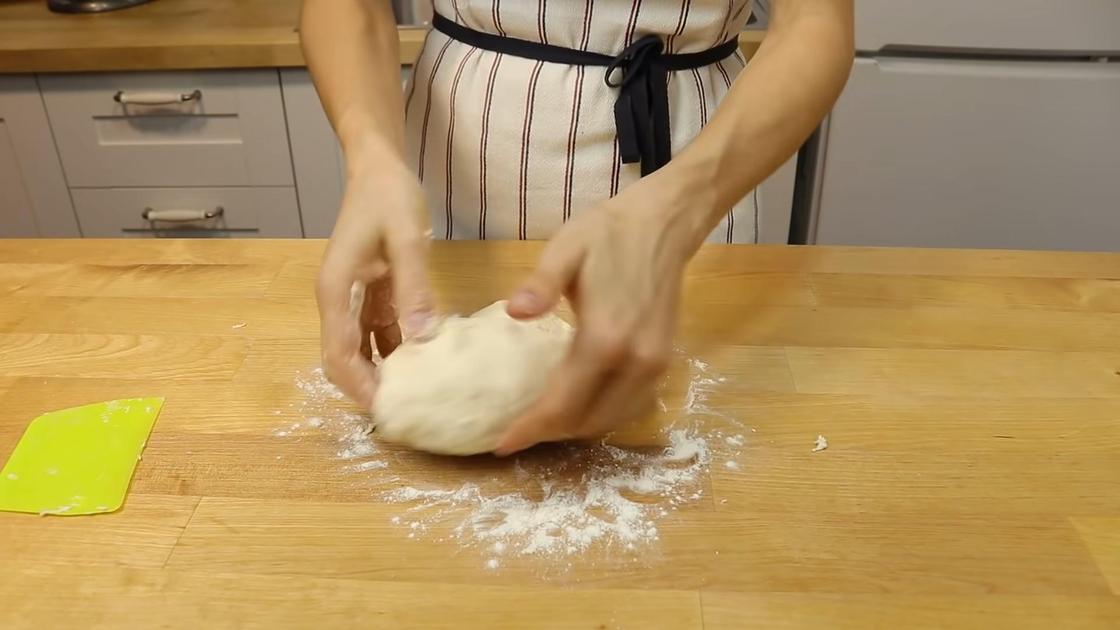 Тесто мешают руками на столе, припыленном мукой