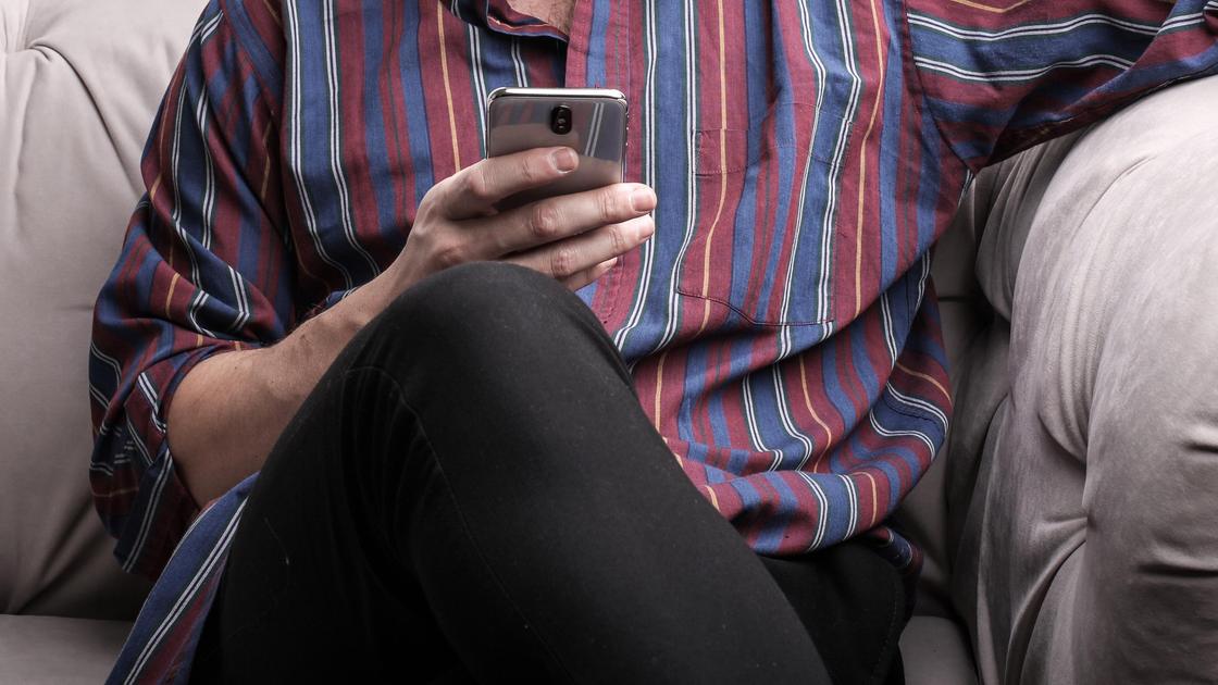 Мужчина сидит на диване с телефоном в руке