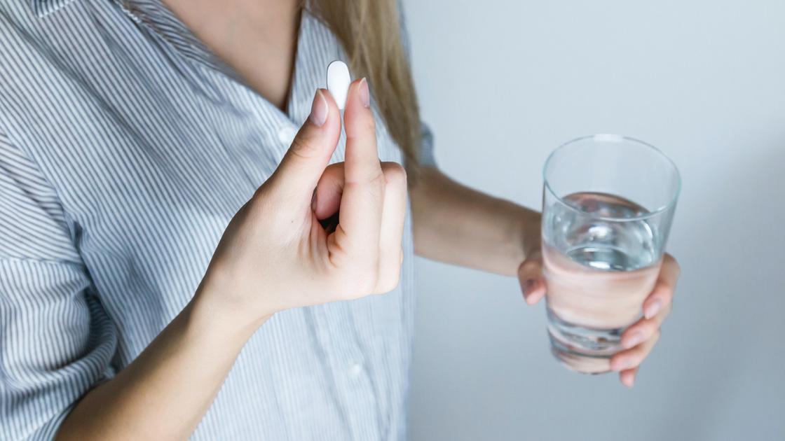 Девушка держит таблетку и стакан воды