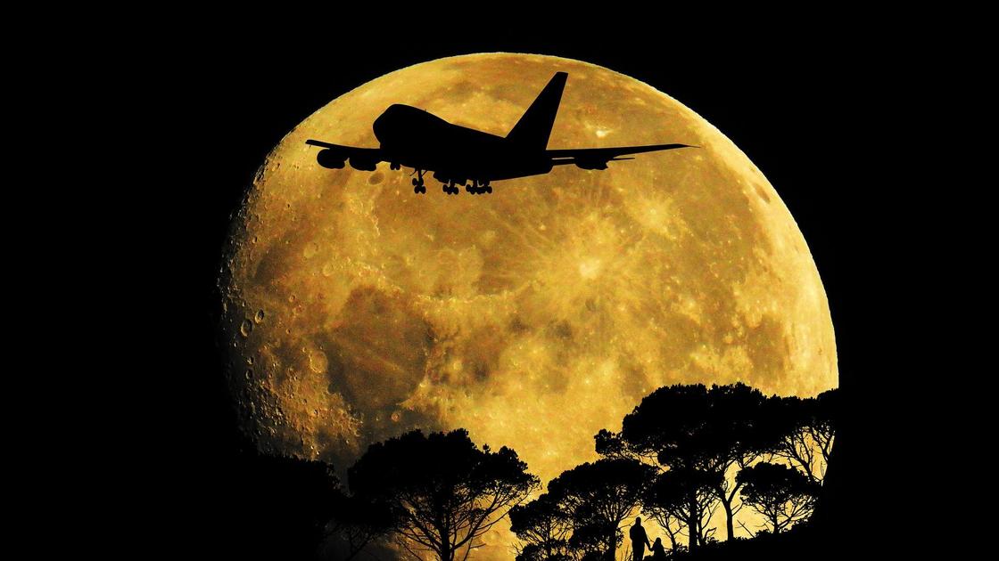 Самолет летит на фоне полной Луны