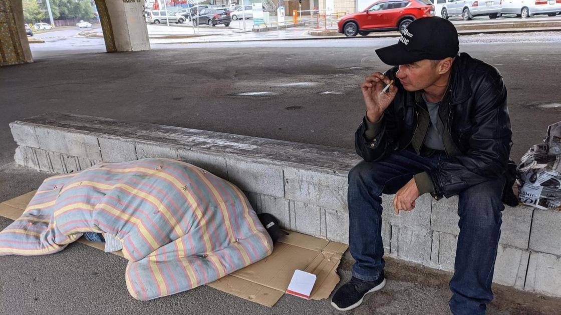 Бездомный мужчина сидит на бордюре в Алматы